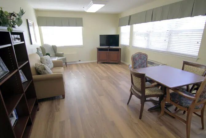 A bright living room with wooden flooring, featuring a television, chairs, and a table.