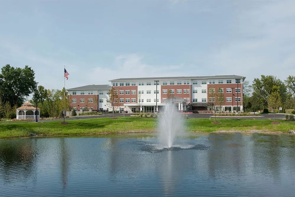 A building with a fountain in front, set beside a pond and surrounded by greenery.