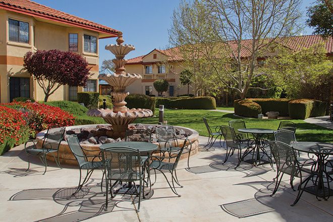 A sunny courtyard with a central fountain, surrounded by outdoor seating and lush landscaping at an apartment complex.