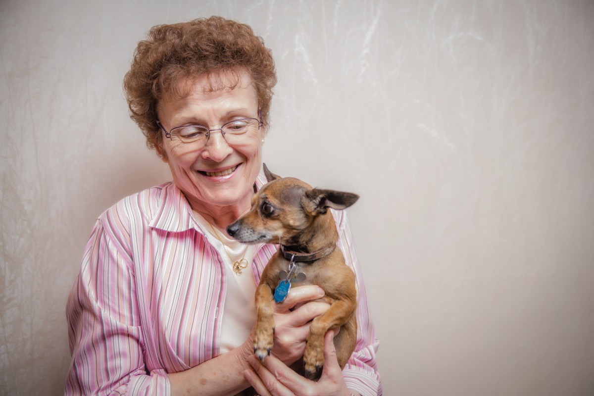 A smiling woman holding her small dog indoors.