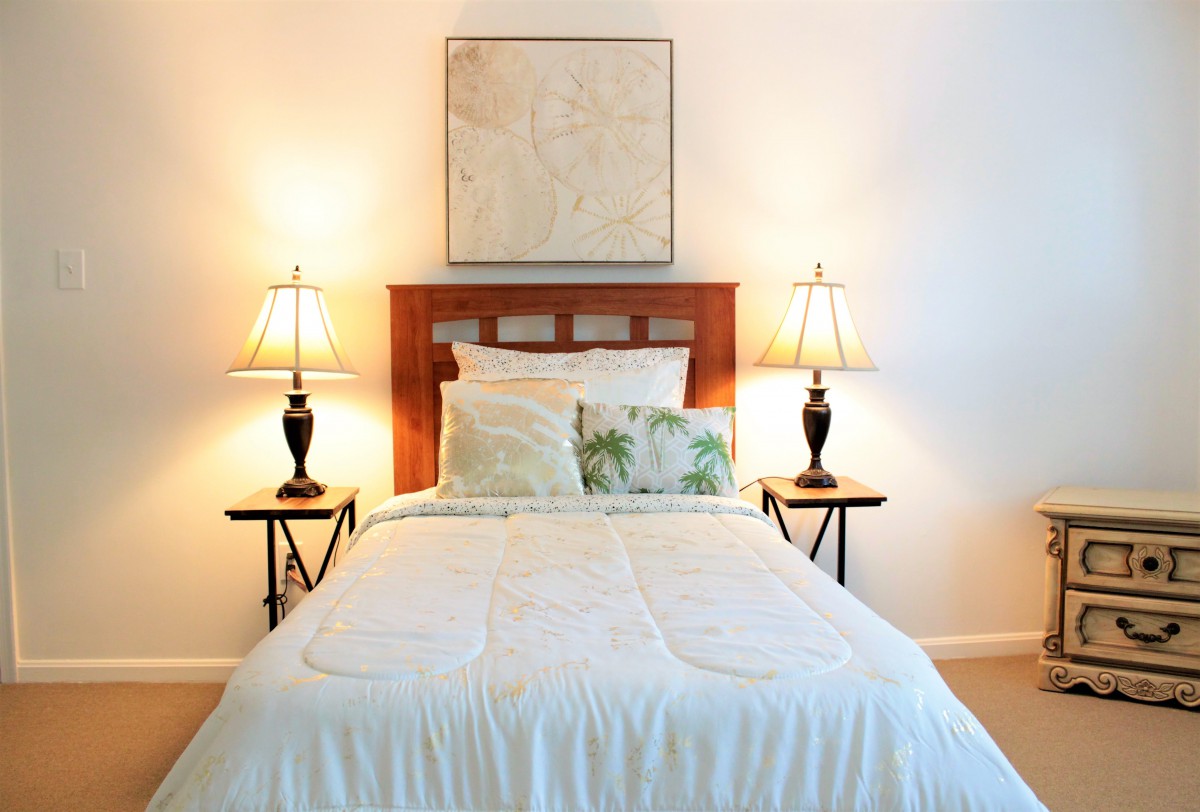 A cozy bedroom with a neatly made bed, flanked by side tables and lamps, featuring simple decor.