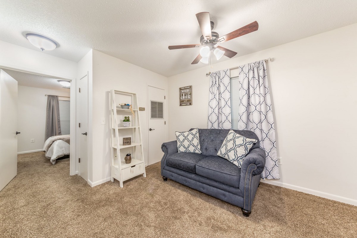 A cozy living room with a blue sofa, patterned curtains, and a ceiling fan.