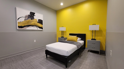 A modern bedroom featuring a yellow accent wall, sleek furniture, and contemporary artwork.