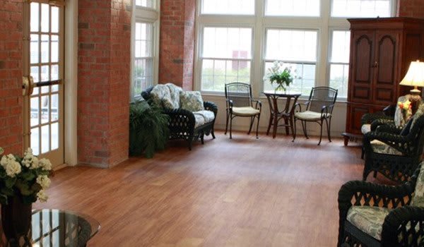 A cozy indoor space with a wicker sofa, a small round table with two chairs, and large windows allowing natural light to fill the room.