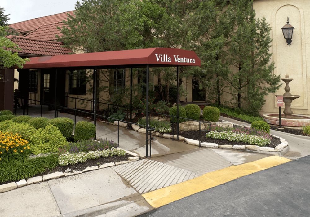 Entrance to a villa with a red awning and landscaped surroundings.