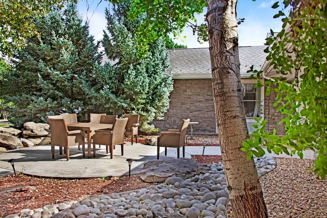 A peaceful backyard patio with outdoor seating surrounded by trees and a rocky garden.