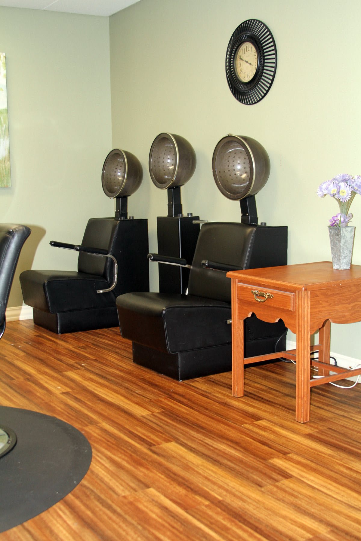 Three hair dryer chairs lined up in a salon with wooden flooring.