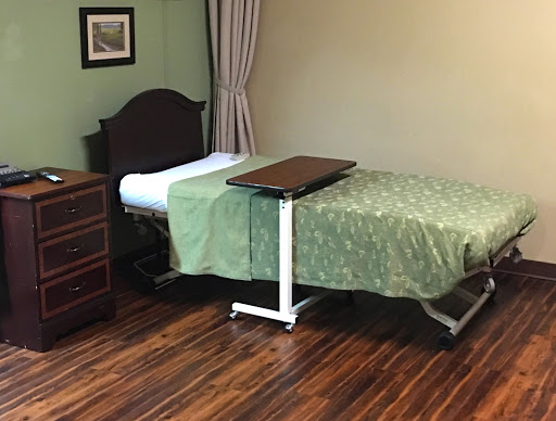 A simple hospital room featuring a medical bed with green bedding and a wooden dresser.