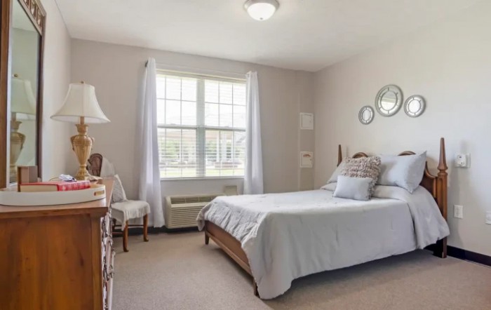 A bright and airy bedroom with a neatly made bed, large window, and simple decor.