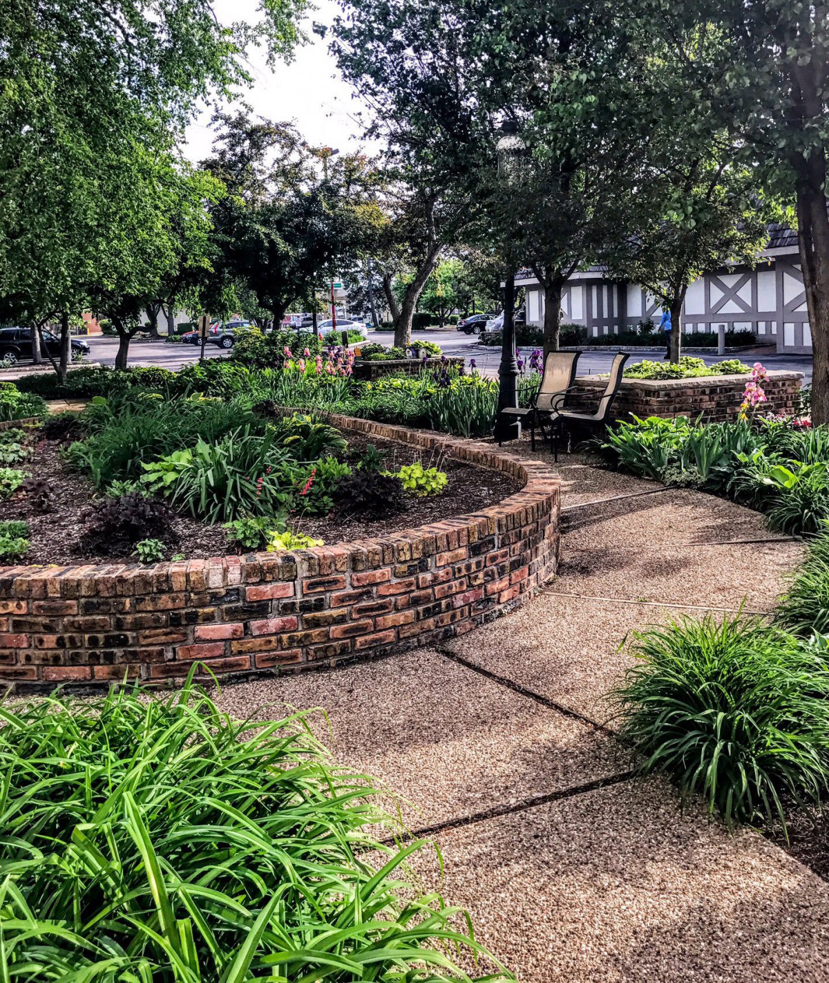 A beautifully landscaped garden featuring a circular brick wall, lush greenery, and a winding pathway.