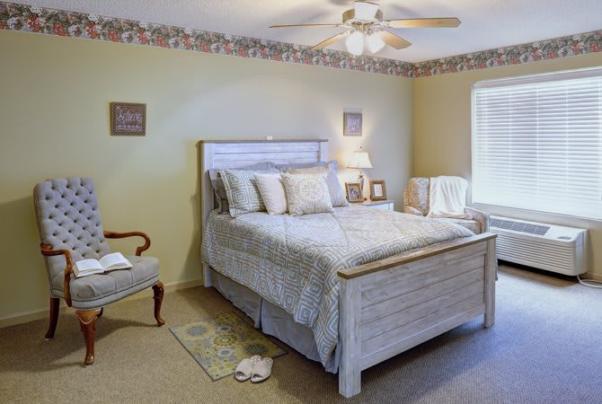 A cozy bedroom with a neatly made bed, accent chairs, and soft lighting.