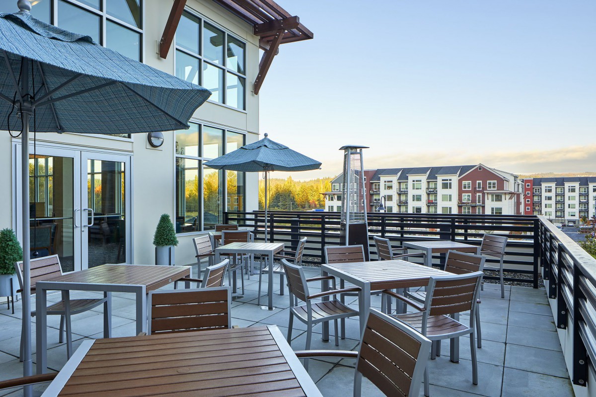 Rooftop patio with tables and umbrellas overlooking a residential area.