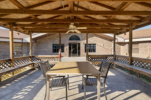 A spacious outdoor patio area featuring a wooden roof, a table with chairs, and a ceiling fan, providing a comfortable space to relax.