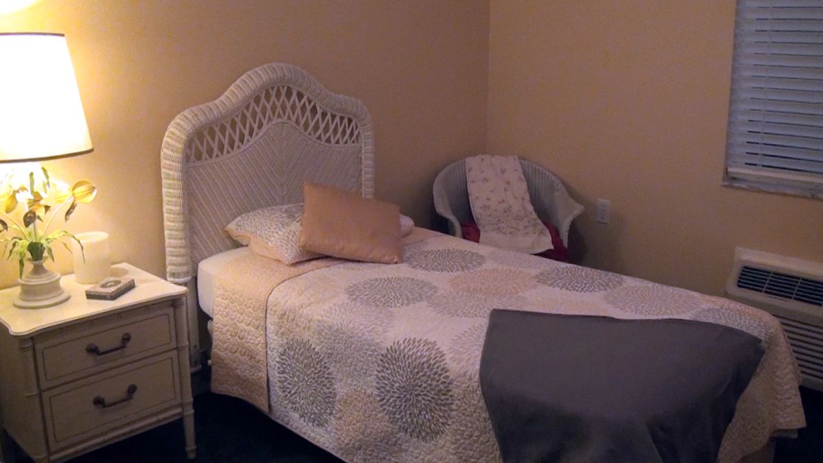 A cozy bedroom with a single bed featuring a wicker headboard and adjacent chair.