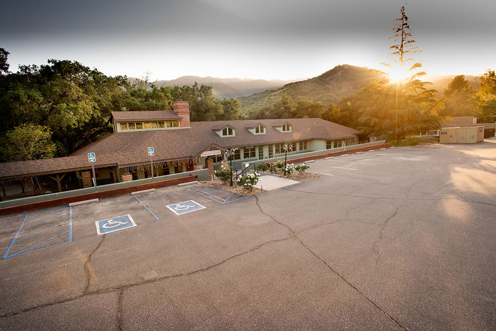 A serene view of a building with an adjacent parking lot, set against a backdrop of mountains at sunset.