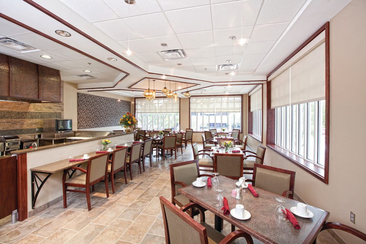 A well-lit restaurant dining area with neatly arranged tables and chairs, featuring a chandelier and large windows.