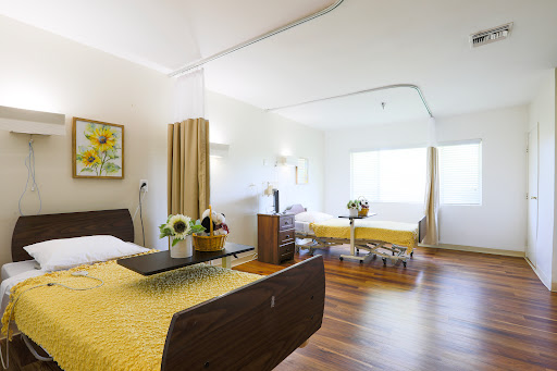 A spacious and well-lit hospital room featuring two beds, modern furnishings, and decorative elements.