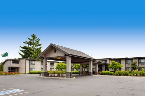 Exterior view of a hotel entrance with a covered canopy and parking area under a clear blue sky.
