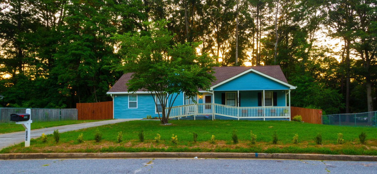 A charming blue house with a porch, surrounded by trees at sunset.