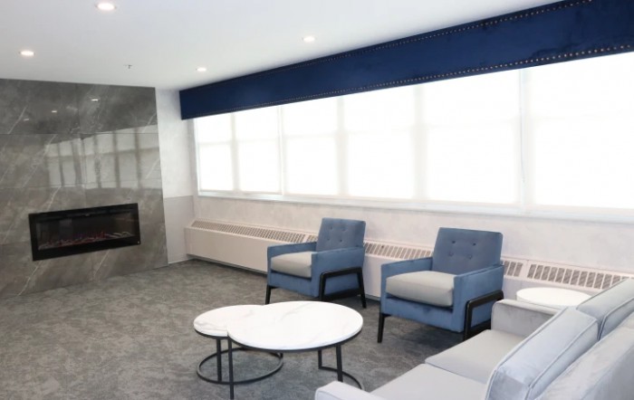 A modern living room with blue chairs, a round coffee table, and large windows.
