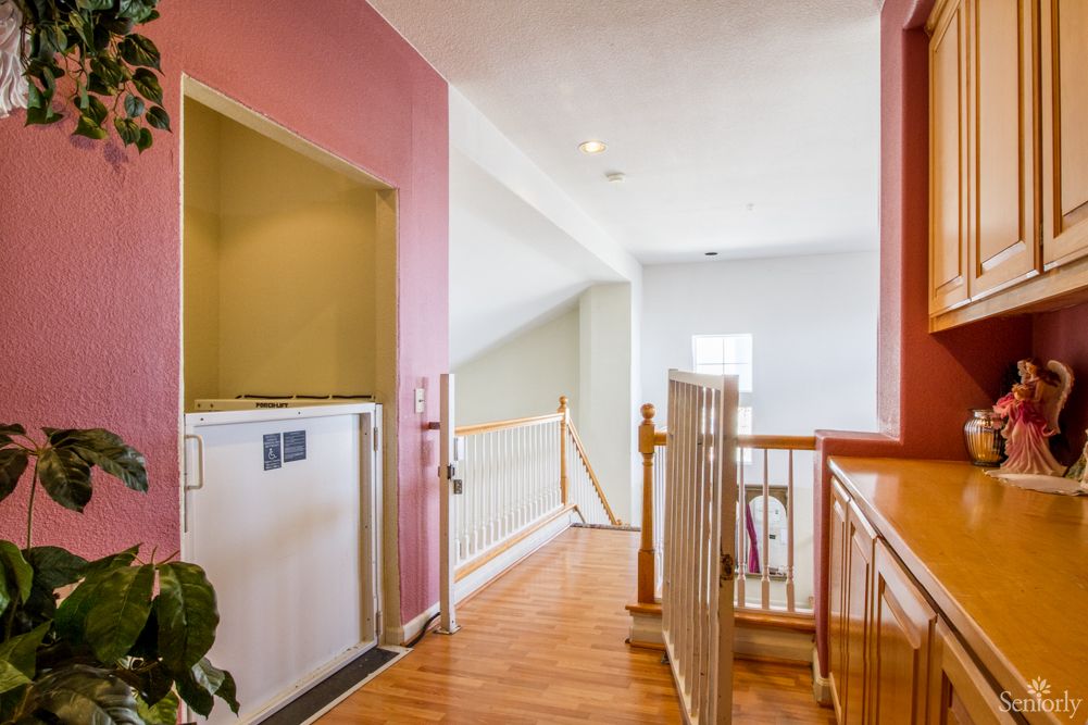 A home hallway featuring a small elevator, wood flooring, and stair railings.