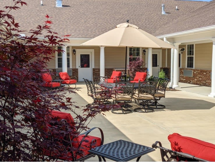 A cozy outdoor patio featuring red-cushioned chairs, tables, and a large umbrella.