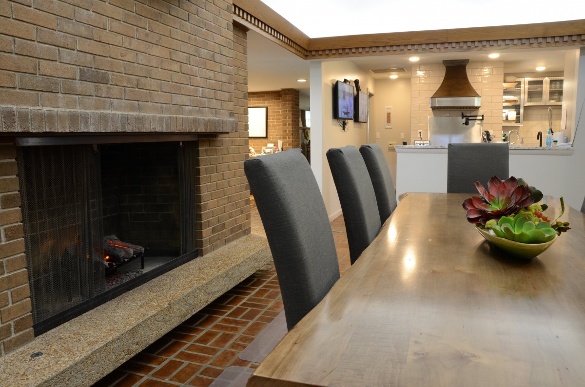 A modern interior featuring a dining area with a fireplace and an adjoining kitchen.