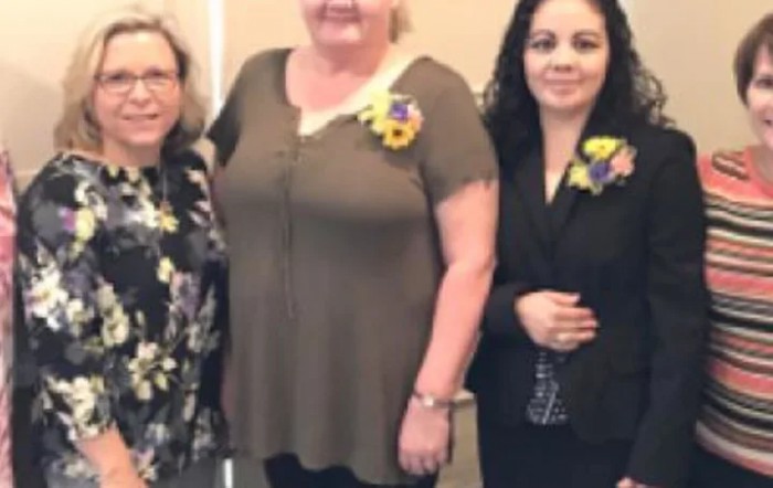 Three women posing together wearing floral pins.