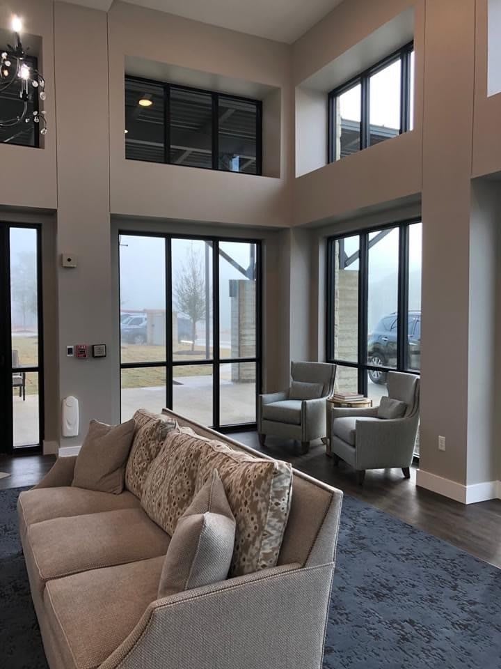 A modern living room with large windows allowing natural light to fill the space, featuring a comfortable sofa and chairs.