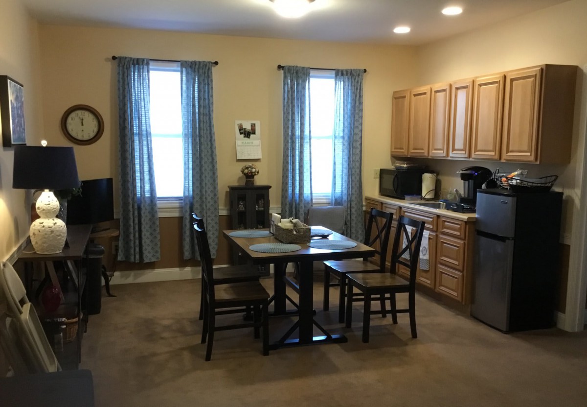 A cozy kitchen with a dining area, featuring wooden cabinets, a small table with four chairs, and blue curtains.