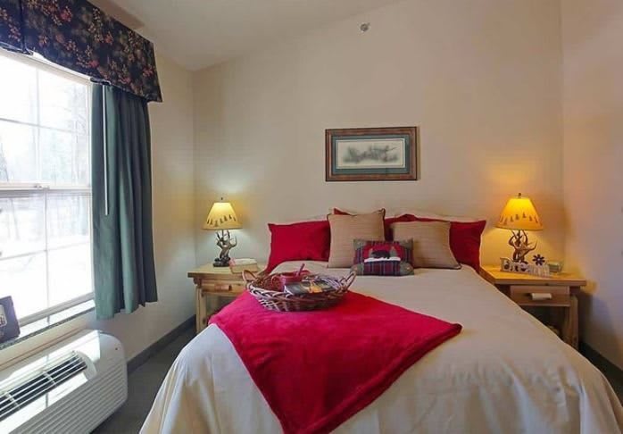 A cozy bedroom with a neatly made bed, adorned with red and beige pillows, flanked by bedside lamps.