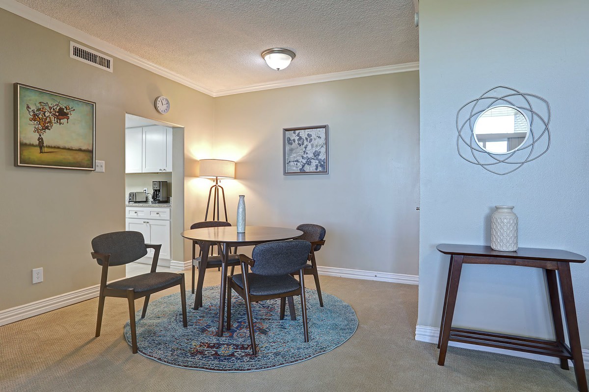 A modern dining room with a round table and stylish chairs, complemented by a floor lamp and wall artwork in a neutral color palette.