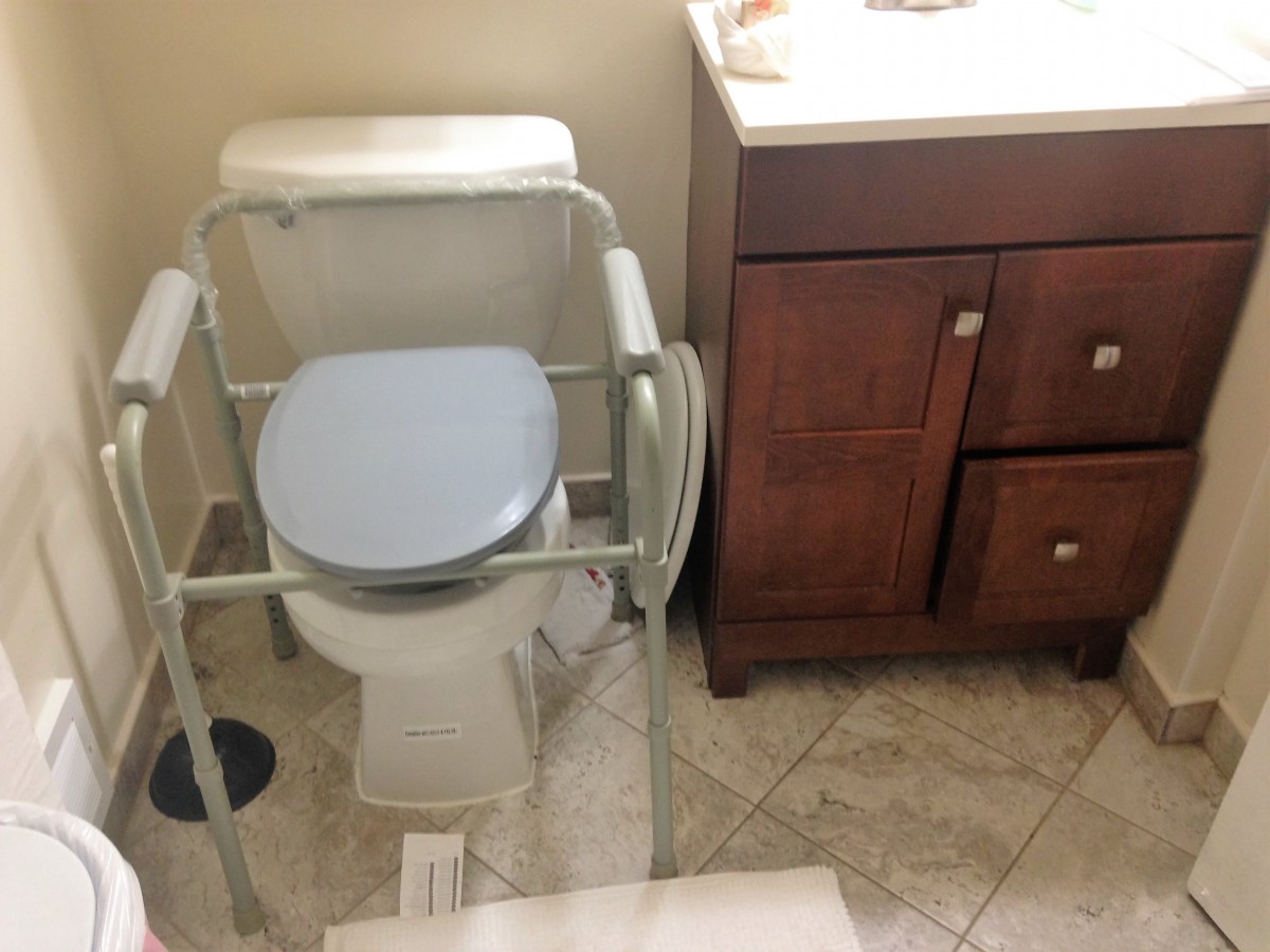 A bathroom with a commode chair over the toilet and a wooden vanity.