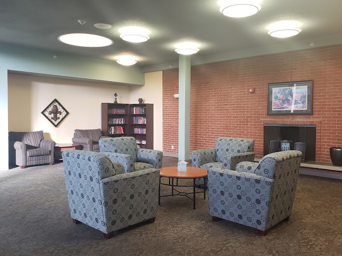 A cozy lounge area with patterned armchairs surrounding a small coffee table, set against a brick wall with a bookshelf and wall art.