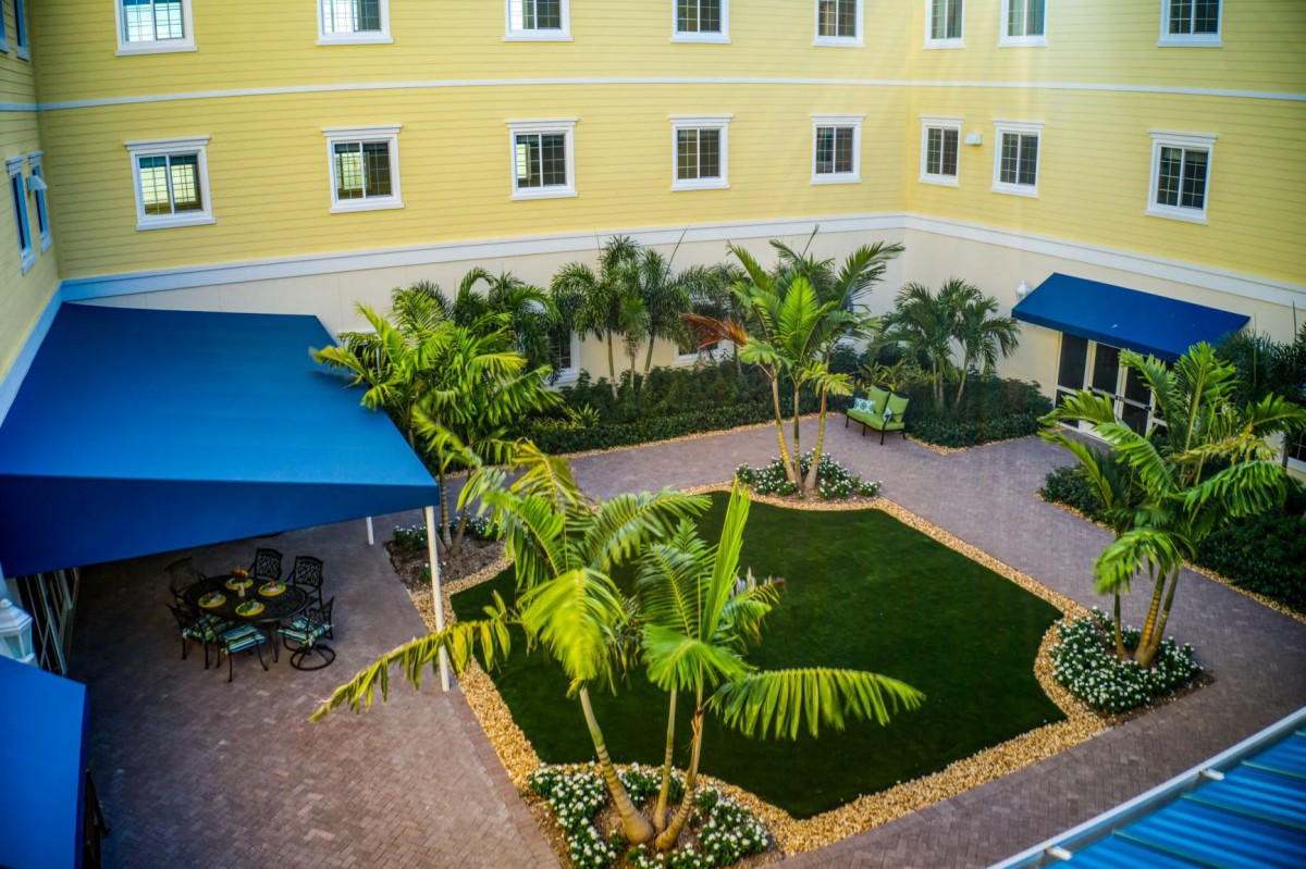 A well-maintained courtyard with palm trees and blue canopies, surrounded by a yellow building with multiple windows.