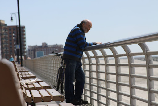 A man with a bicycle leans over the railing of a pier, enjoying the view of the river.