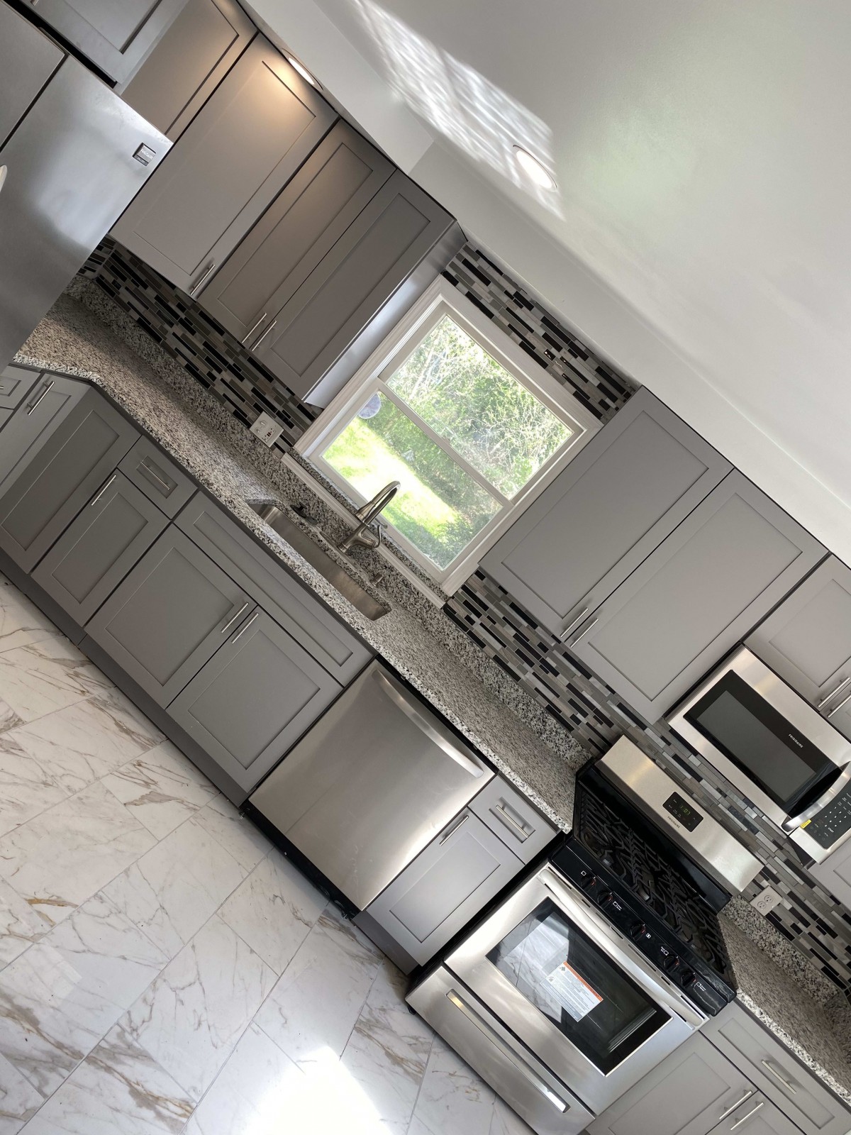 A modern kitchen with gray cabinets, stainless steel appliances, and a marble floor.