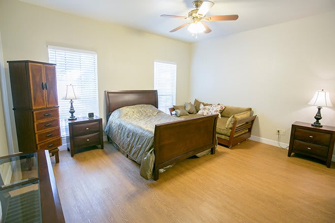 A cozy bedroom with a wooden bed, a couch, and a ceiling fan.