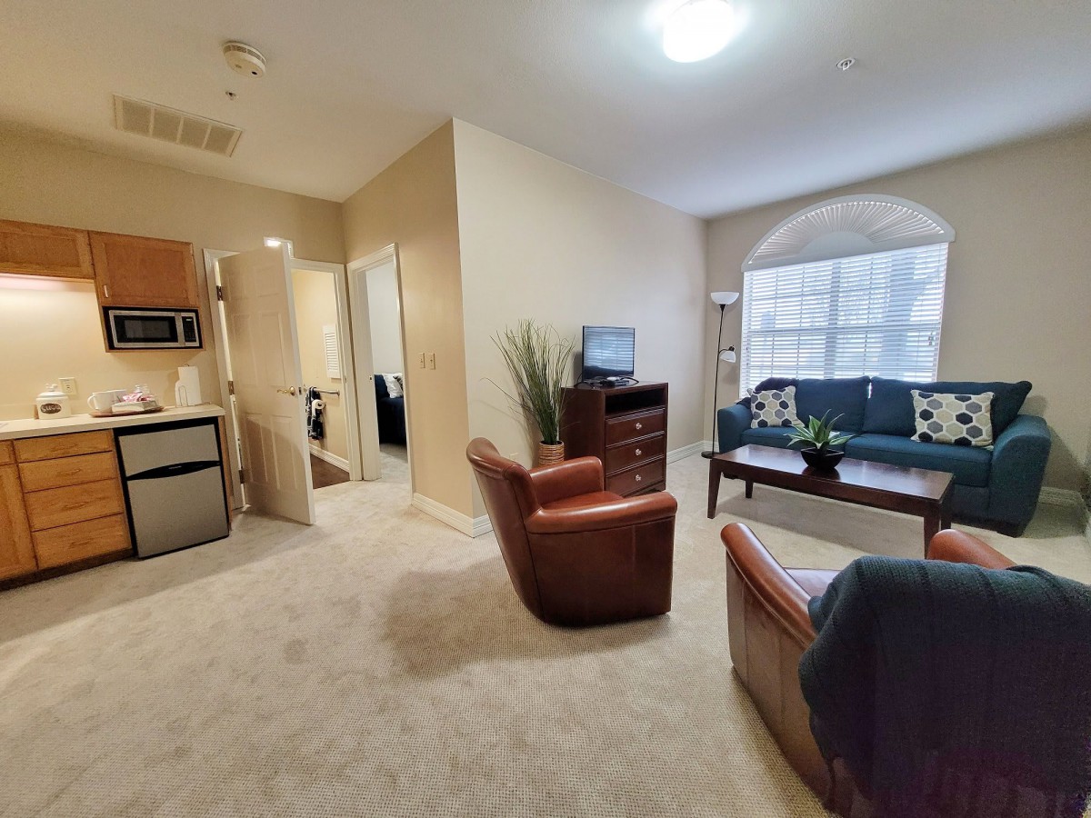 A cozy apartment living room with a connected kitchen space, featuring comfortable seating and a large window.