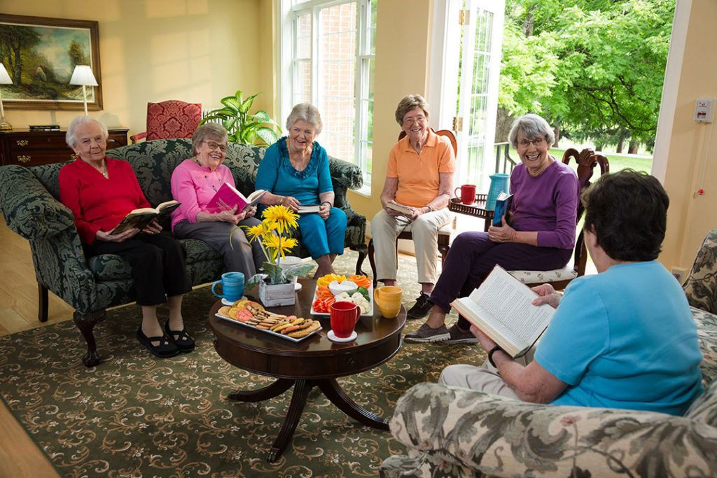 A group of senior women gathered in a living room for a book club meeting.