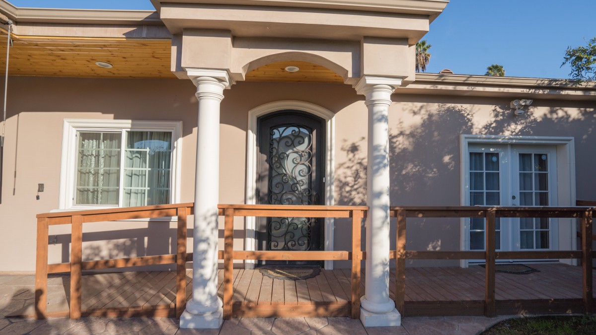 A residential house entrance featuring a decorative front door with white columns and a wooden porch.