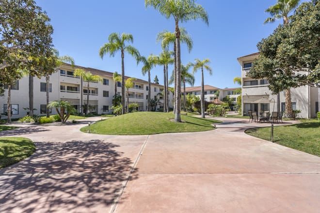 A sunny view of a modern apartment complex surrounded by palm trees and well-maintained landscaping.