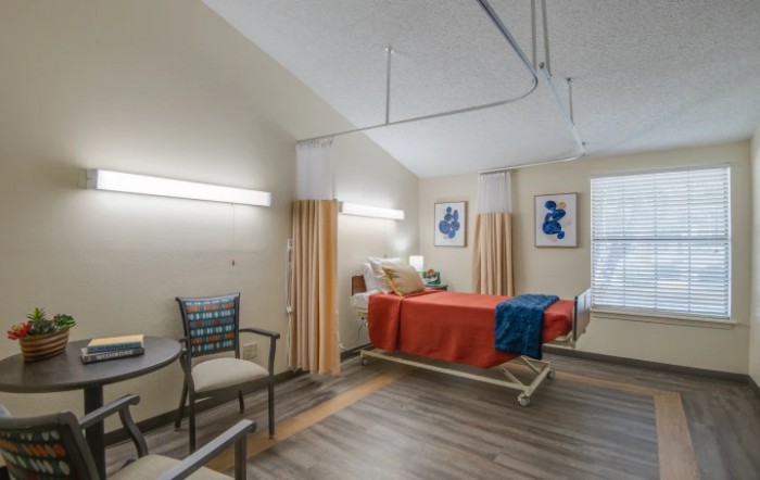 A well-lit hospital room with a single bed, chair, and decorative artwork on the walls.