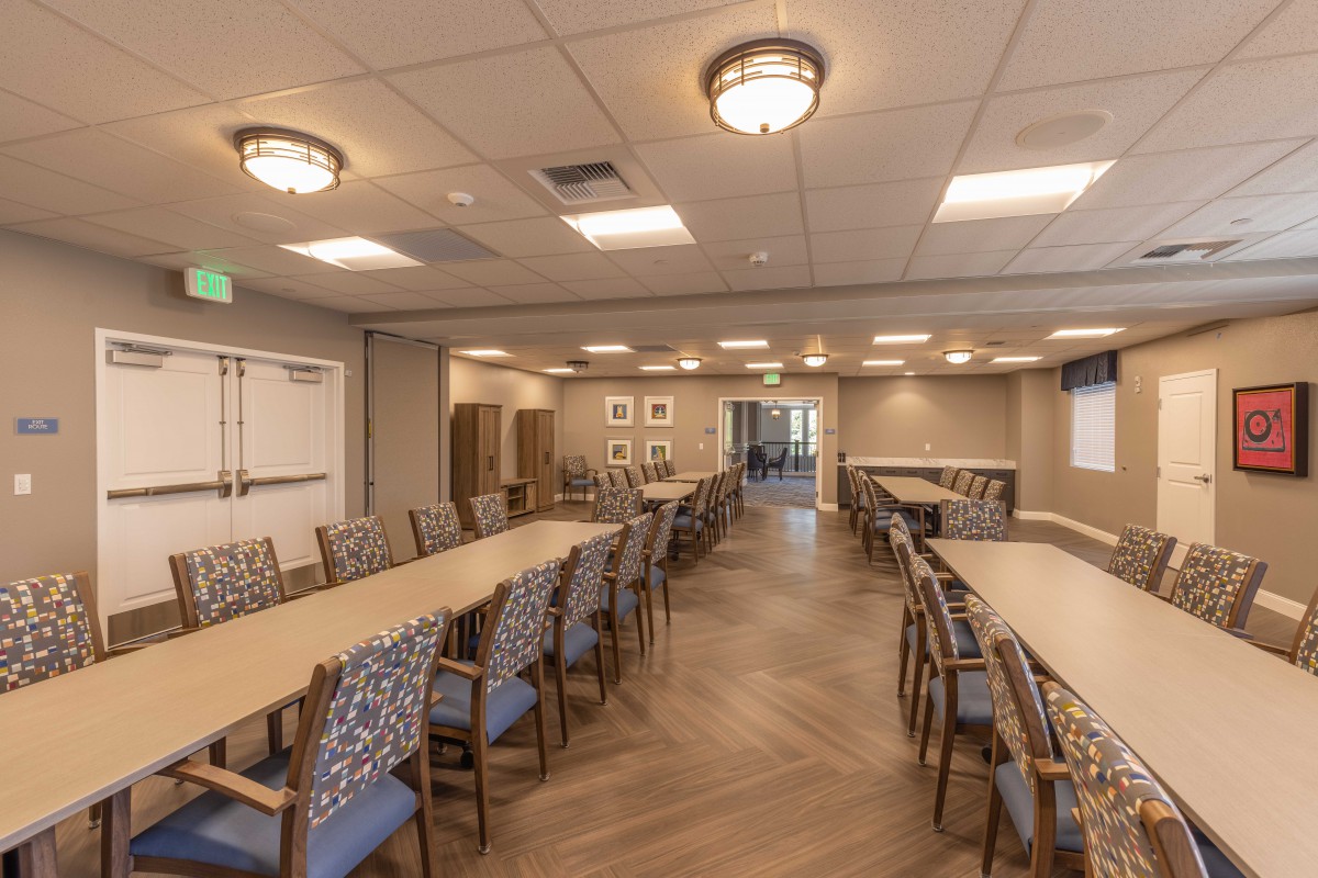 A spacious conference room with arranged tables and chairs, featuring ceiling lights and wall decor.