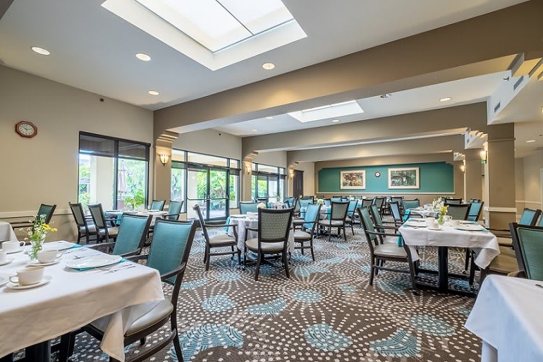 A spacious and elegantly designed dining area with tables and chairs, featuring modern lighting and large windows.