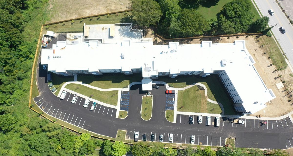 Aerial view of a building with a parking lot and surrounding greenery.