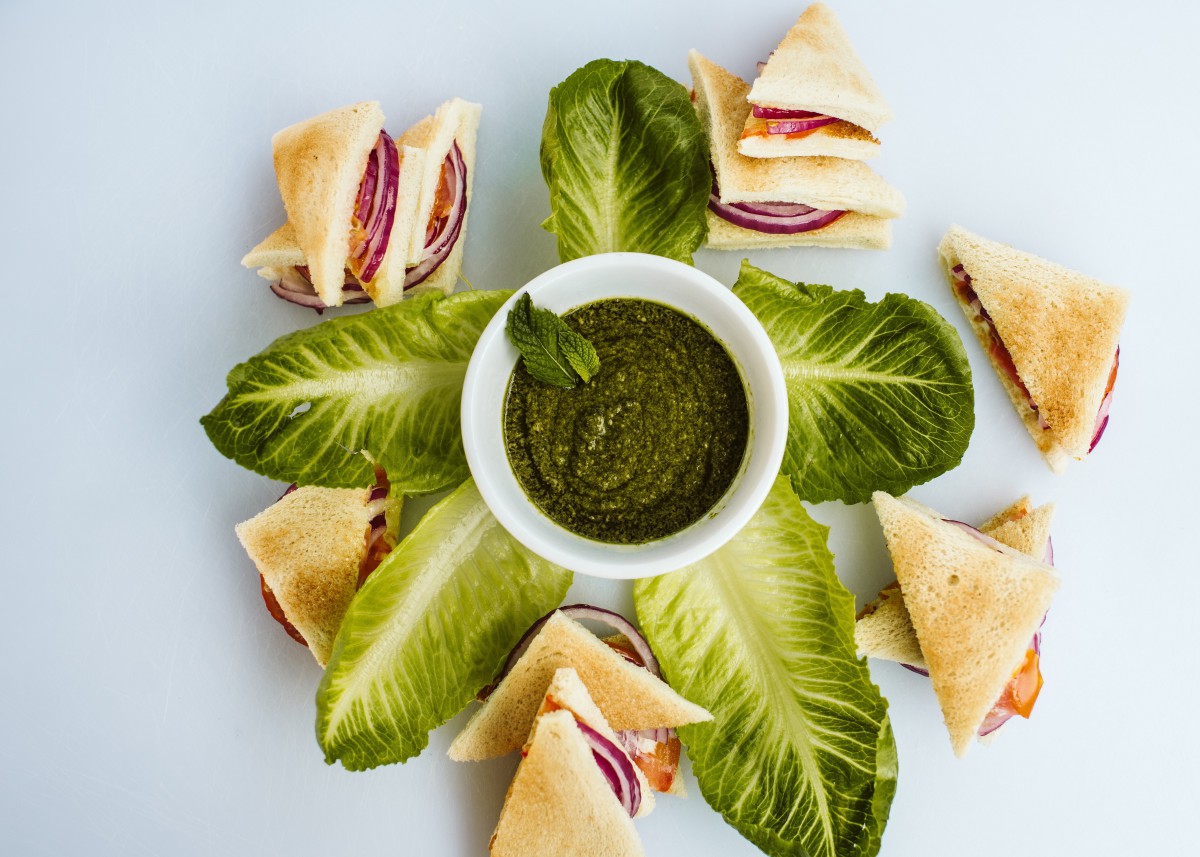 A beautifully arranged platter featuring pita sandwiches with a green dipping sauce, garnished with fresh lettuce leaves.