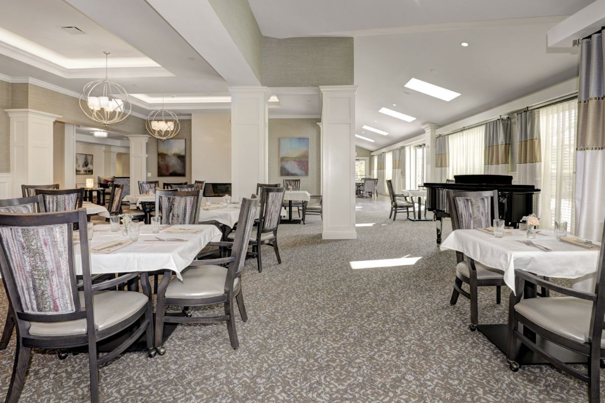 A spacious and elegantly decorated dining room with multiple tables and chairs, illuminated by chandeliers.