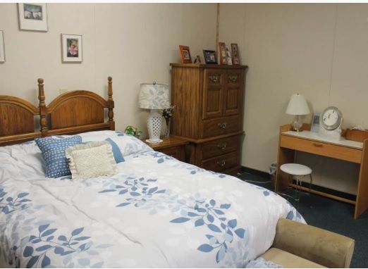 A cozy bedroom with wooden furniture, featuring a bed with floral bedding, a dresser, and a small desk with lamps.
