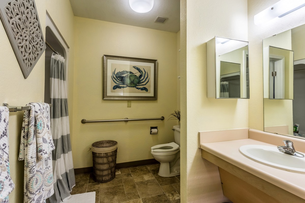 A well-lit bathroom featuring a toilet, sink, mirror, and a framed artwork on the wall.